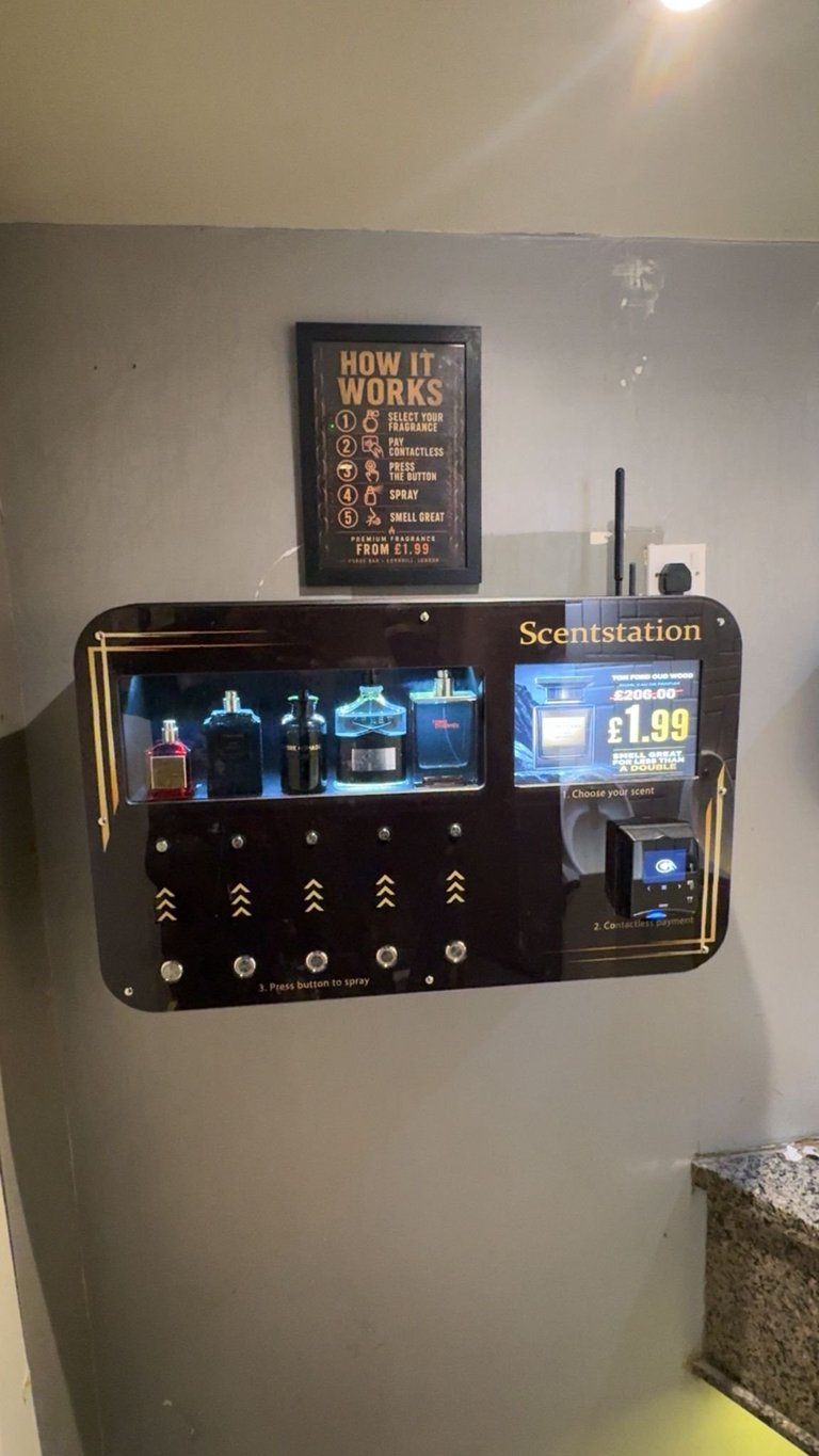 Wall-mounted black Scentstation fragrance dispenser with illuminated product display and instruction sign above